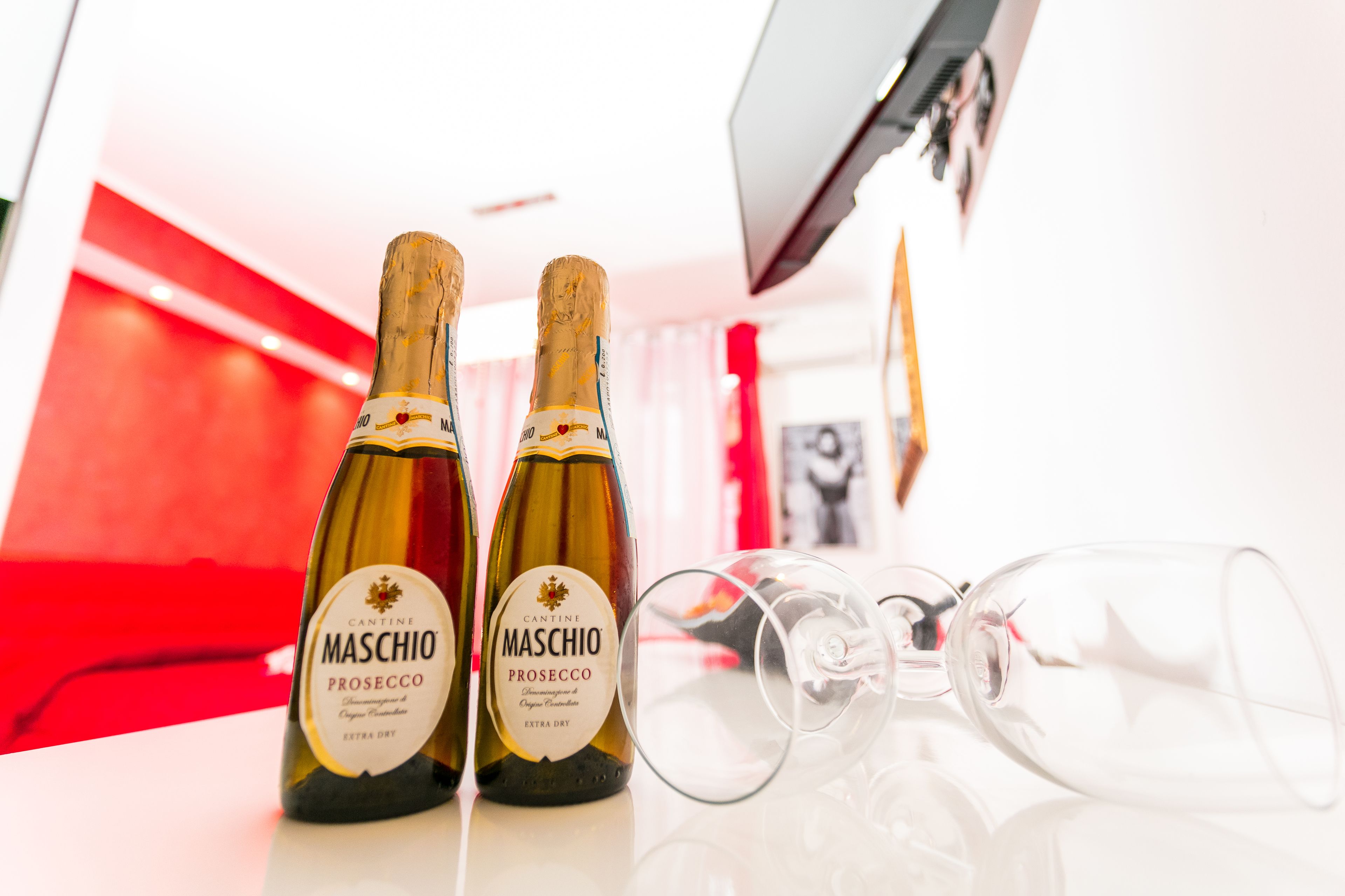 Zwei Flaschen Maschio Prosecco und drei leere Weingläser auf einer spiegelnden Oberfläche.