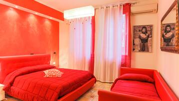 A room with a red bed, a smaller red chair, a nightstand, and a mirror on the wall.