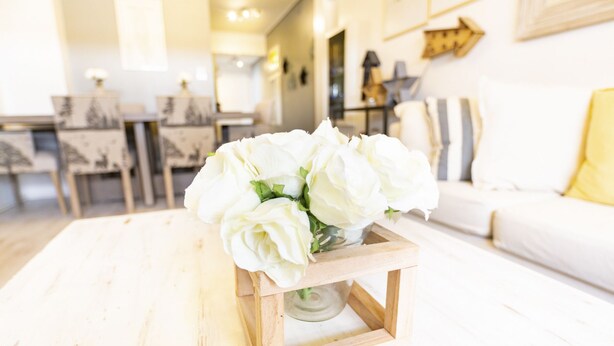 A white living room with a wooden coffee table holding a vase of white flowers.