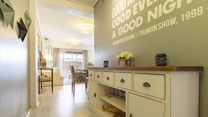A hallway with a white cabinet, a dining area with a table and chairs, and a wall with a light fixture.
