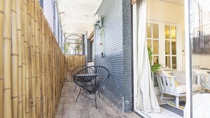 A narrow outdoor corridor with a bamboo fence, a black wire chair, and a tiled wall.