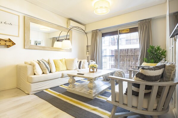 A modern living room with a white sofa, a wooden coffee table, a white armchair, and a large mirror on the wall.