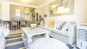A modern living room with a white sofa, a wooden coffee table, and a dining area with chairs and a table.