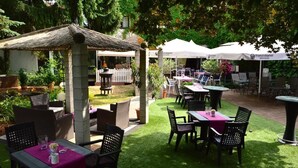 An outdoor patio area with tables and chairs, a thatched-roof structure, and umbrellas. - Hotel Haus Krone (Bexbach)