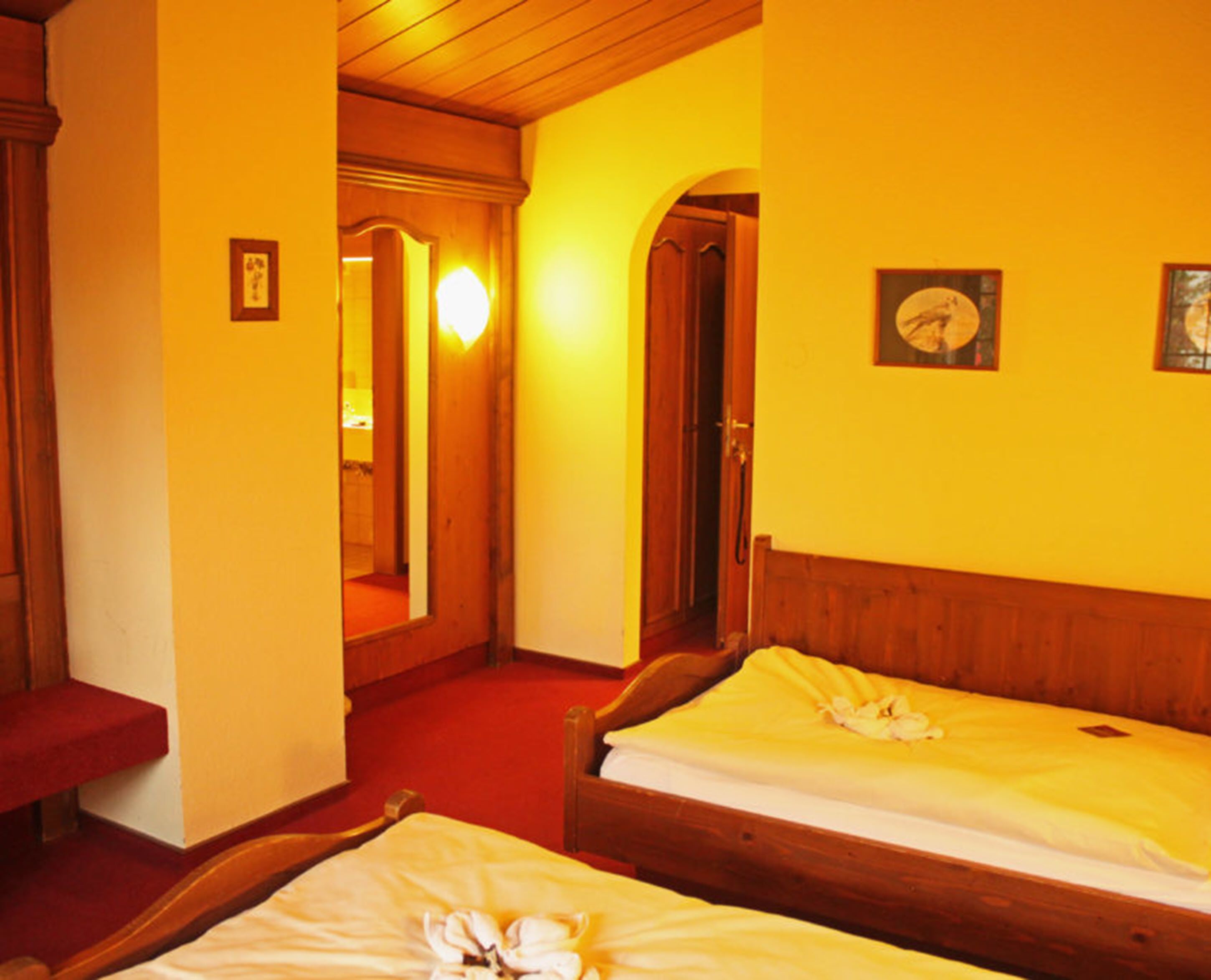 A hotel room with two wooden beds, a red carpet, and a mirror on the wall.