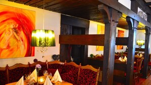 A restaurant with a wooden bench seating area, a table set for two, and a large abstract painting on the wall. - Hotel Haus Krone (Bexbach)