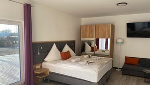 A modern hotel room with a large bed, a seating area, a TV, and a window with curtains. - Hotel Haus Krone (Bexbach)