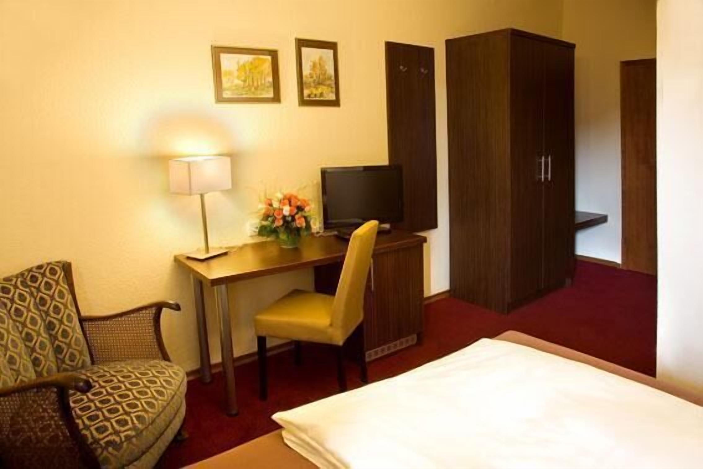 A hotel room with a bed, a desk with a television, a chair, and a wardrobe.