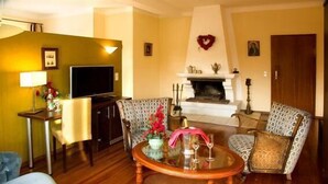 A living room with a fireplace, two patterned armchairs, a round coffee table, a television, and a small table with a lamp and flowers. - Hotel Haus Krone (Bexbach)