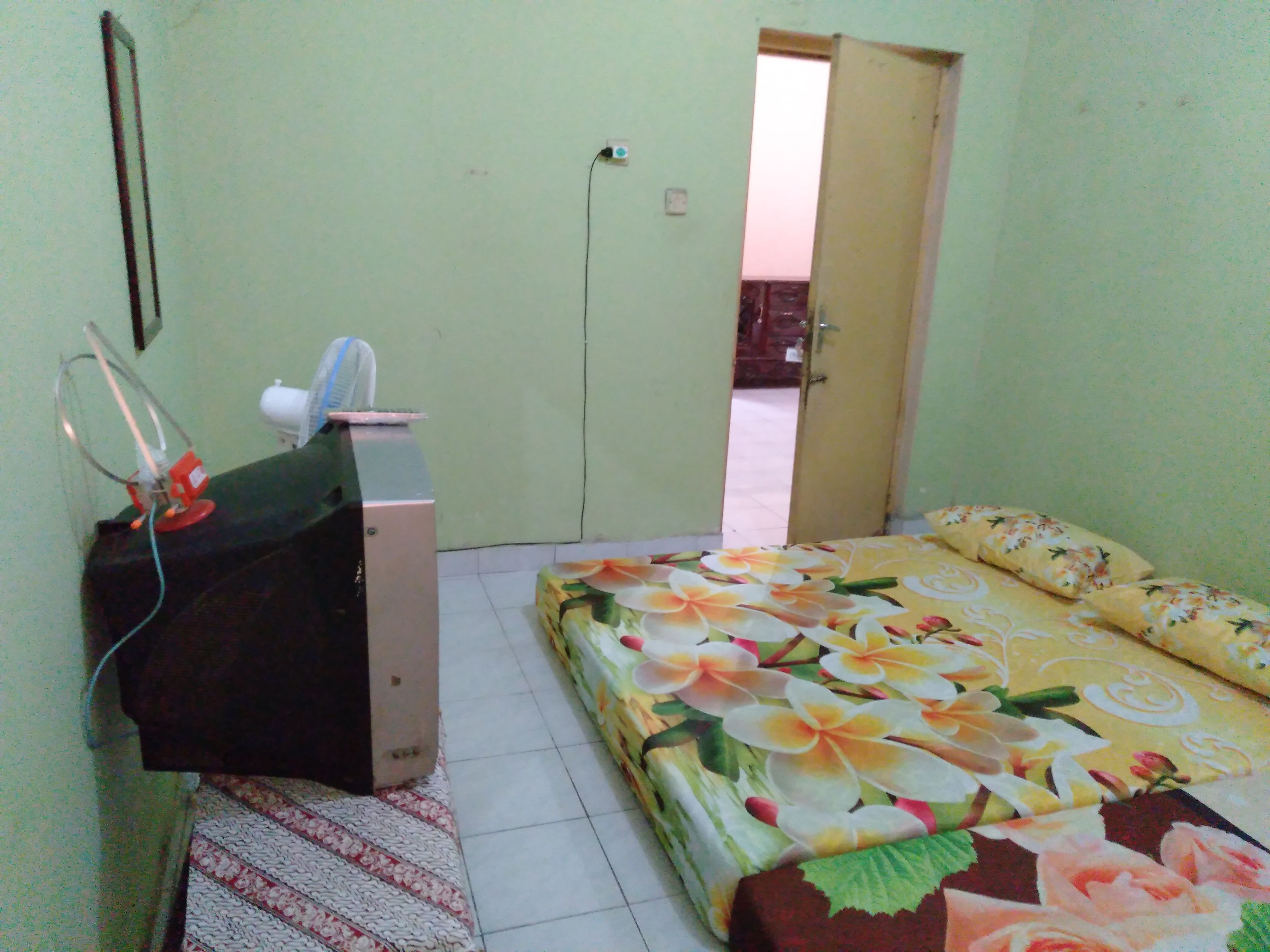 A room with a bed, a desk with a computer, and a door leading to another room.