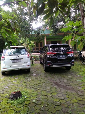 Two parked cars on a cobblestone path with a building in the background. - Setro Kariyo Homestay (Srimulyo)