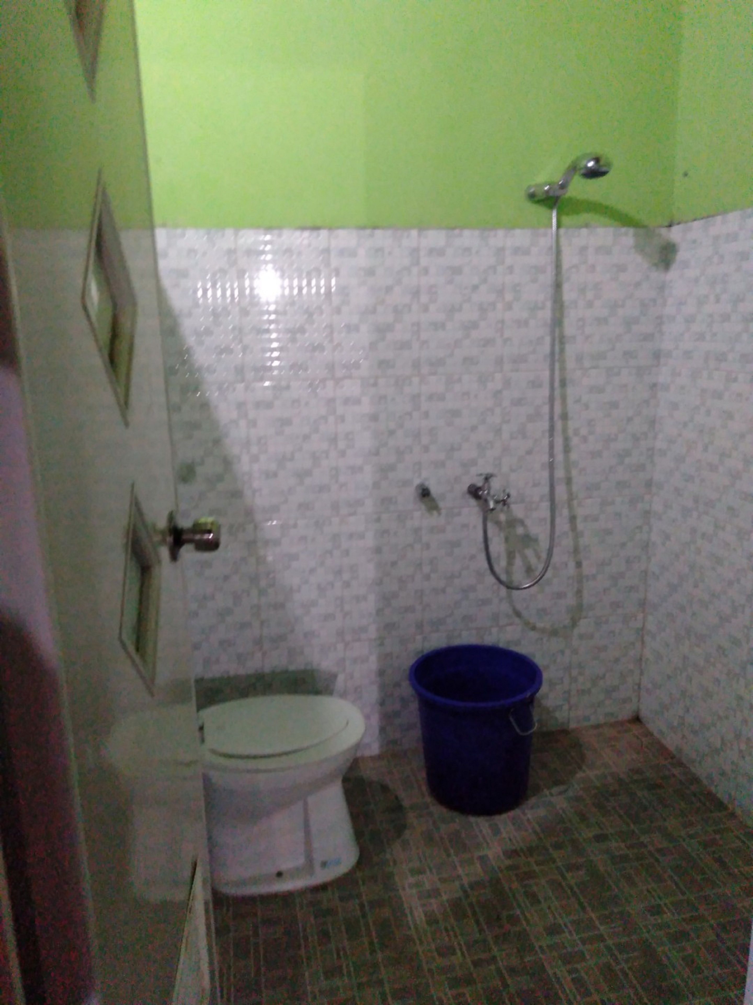 A small bathroom with a toilet, a shower, and a blue bucket.