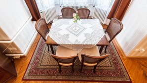 A dining area with a round table covered by a lace tablecloth, surrounded by four wicker chairs with cushioned seats.