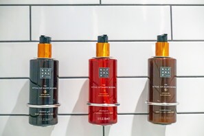 Three bottles of Ritual of Happy Buddha products: shower gel, shampoo, and conditioner, arranged on a tiled wall. - The Hendrick Smithfield (Dublin)