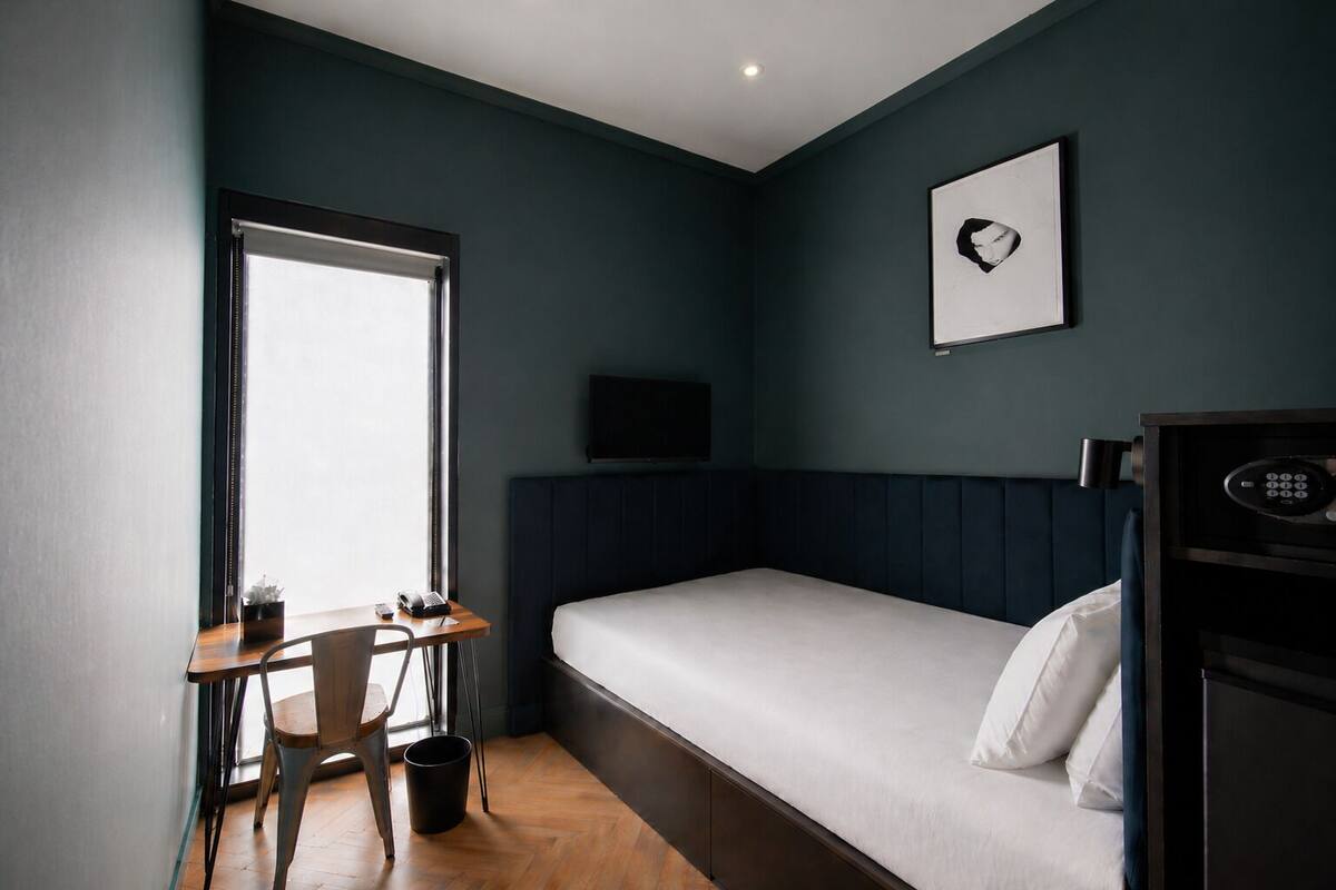 A compact hotel room with a single bed, a desk with a chair, a television, and a window.