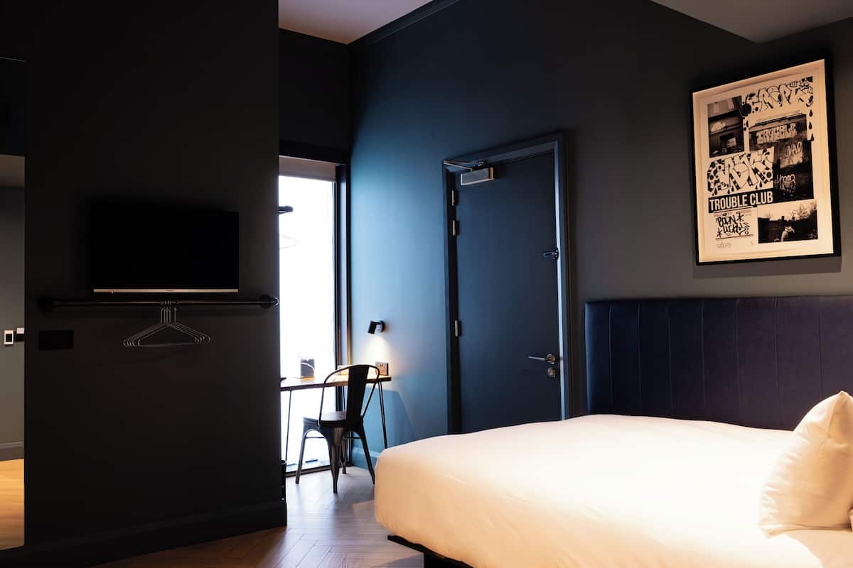 A hotel room with a bed, a desk with a chair, a television, and a door.