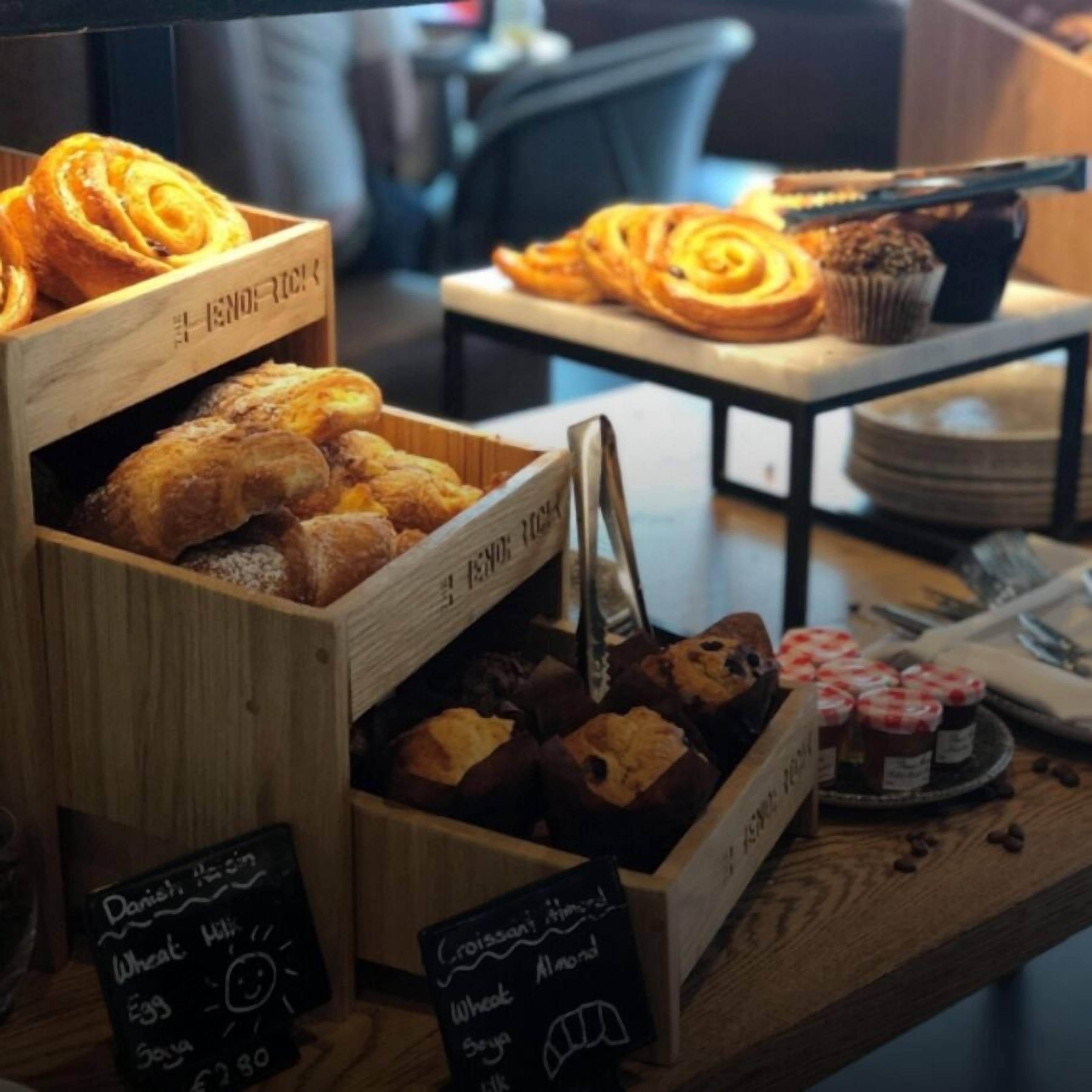 Mostrador de panadería con diversas opciones horneadas, incluyendo pasteles y pan, dispuestas sobre puestos de madera.