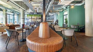 A modern interior with a central seating area, tables, and chairs, surrounded by large windows and a green accent wall.