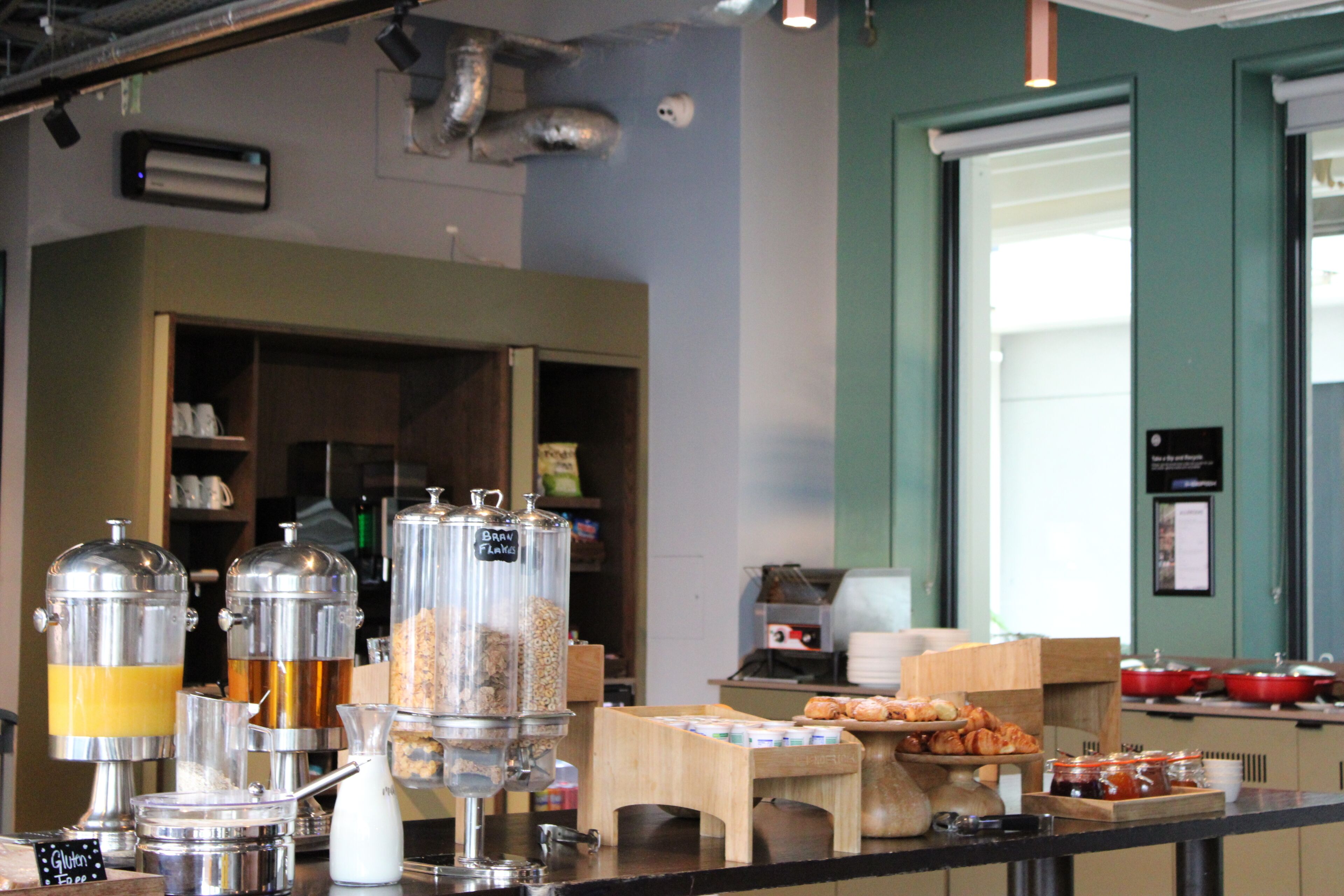A breakfast buffet setup with various food dispensers and a coffee station.