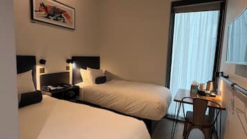 A hotel room with two beds, a desk, a chair, a window with curtains, a painting on the wall, and a ceiling light fixture.