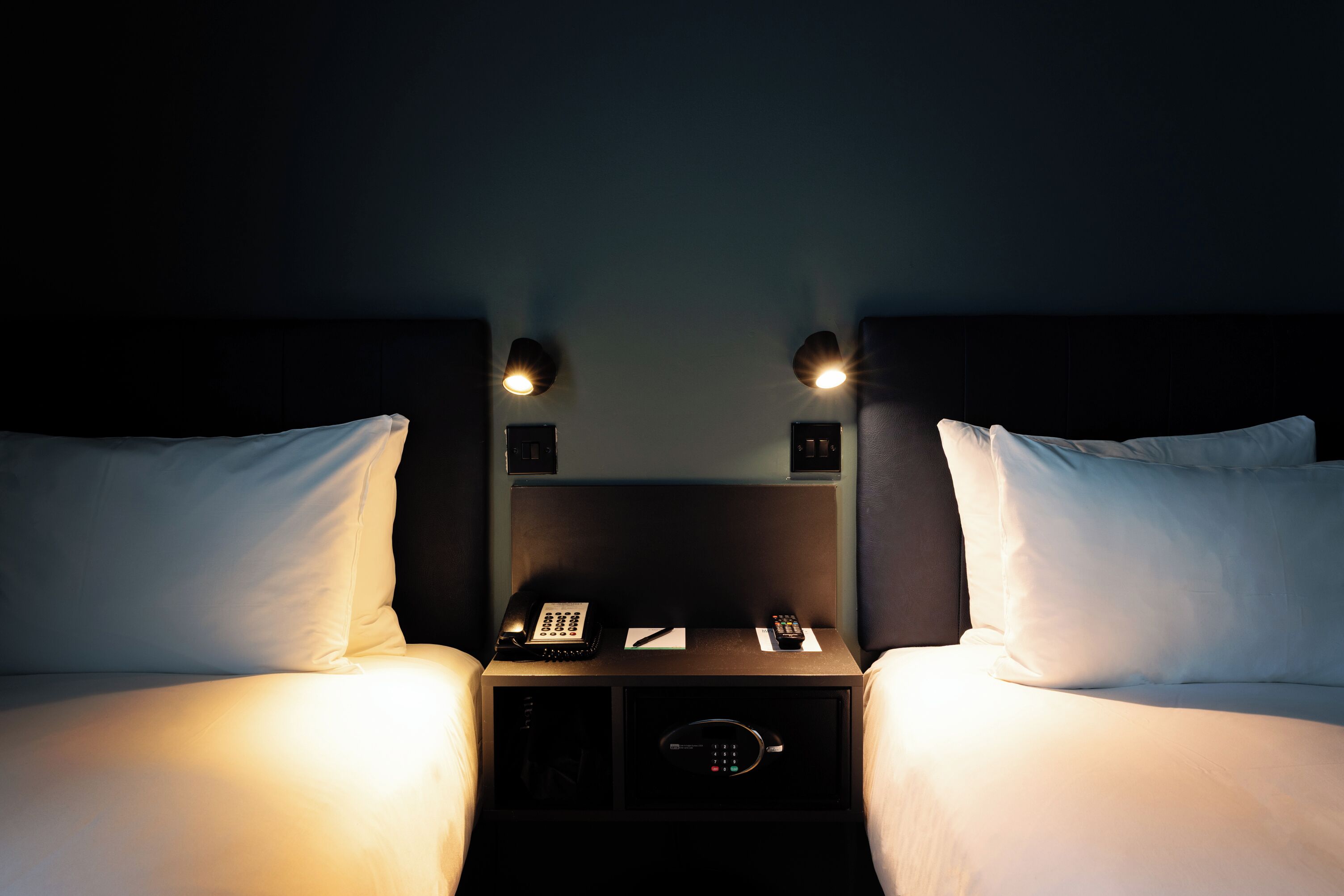 A hotel room with two beds, bedside lamps, a phone, and a safe.
