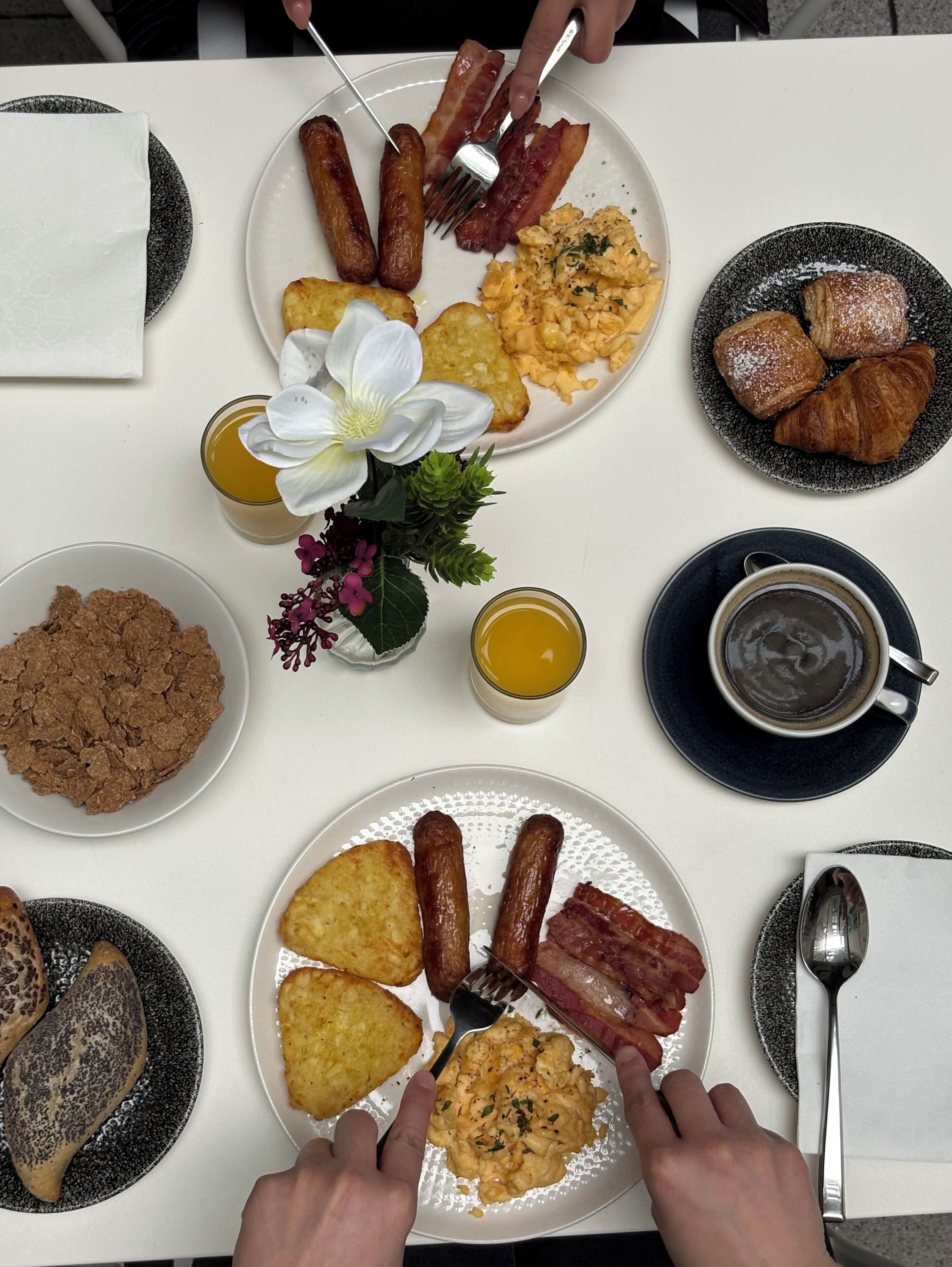 A breakfast table with plates of food, a flower arrangement, and a cup of coffee.