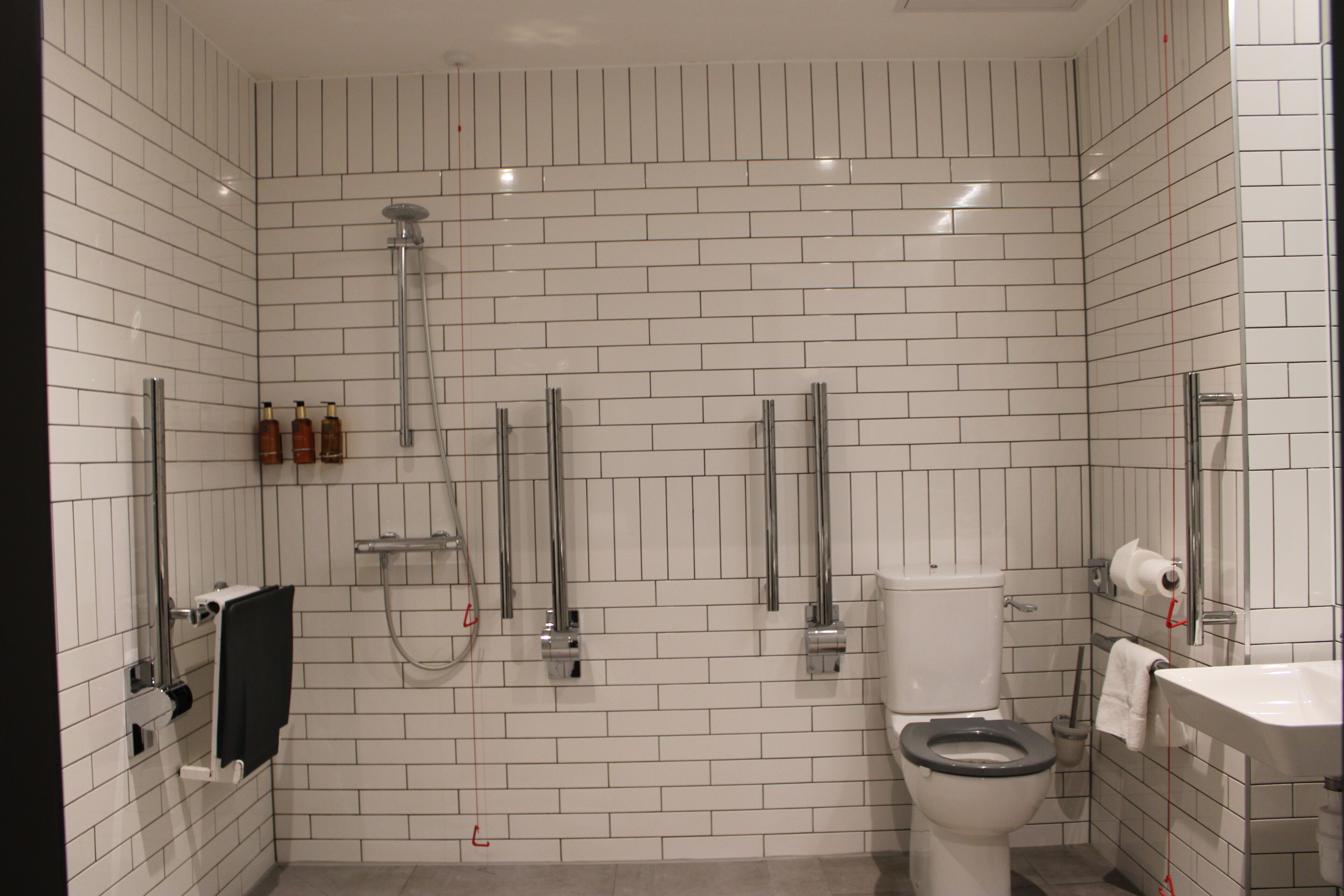 Un baño con paredes de azulejos blancos, un inodoro, una zona de ducha y un lavabo.