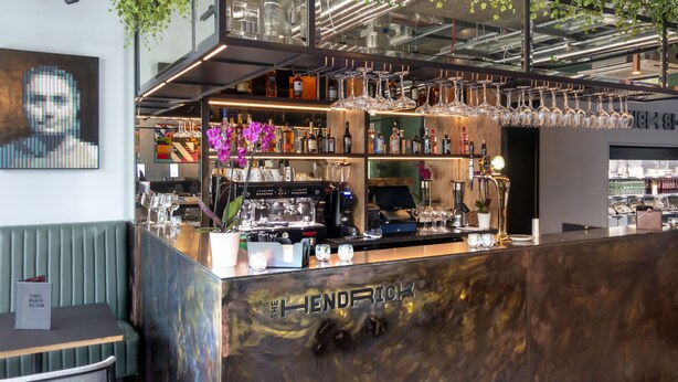 Zona de bar con mostrador, estanterías llenas de botellas y copas colgantes.