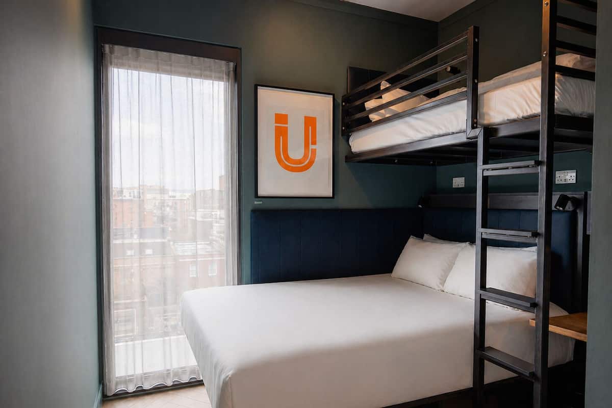 A bunk bed room with a bed, a window with curtains, and a framed picture on the wall.