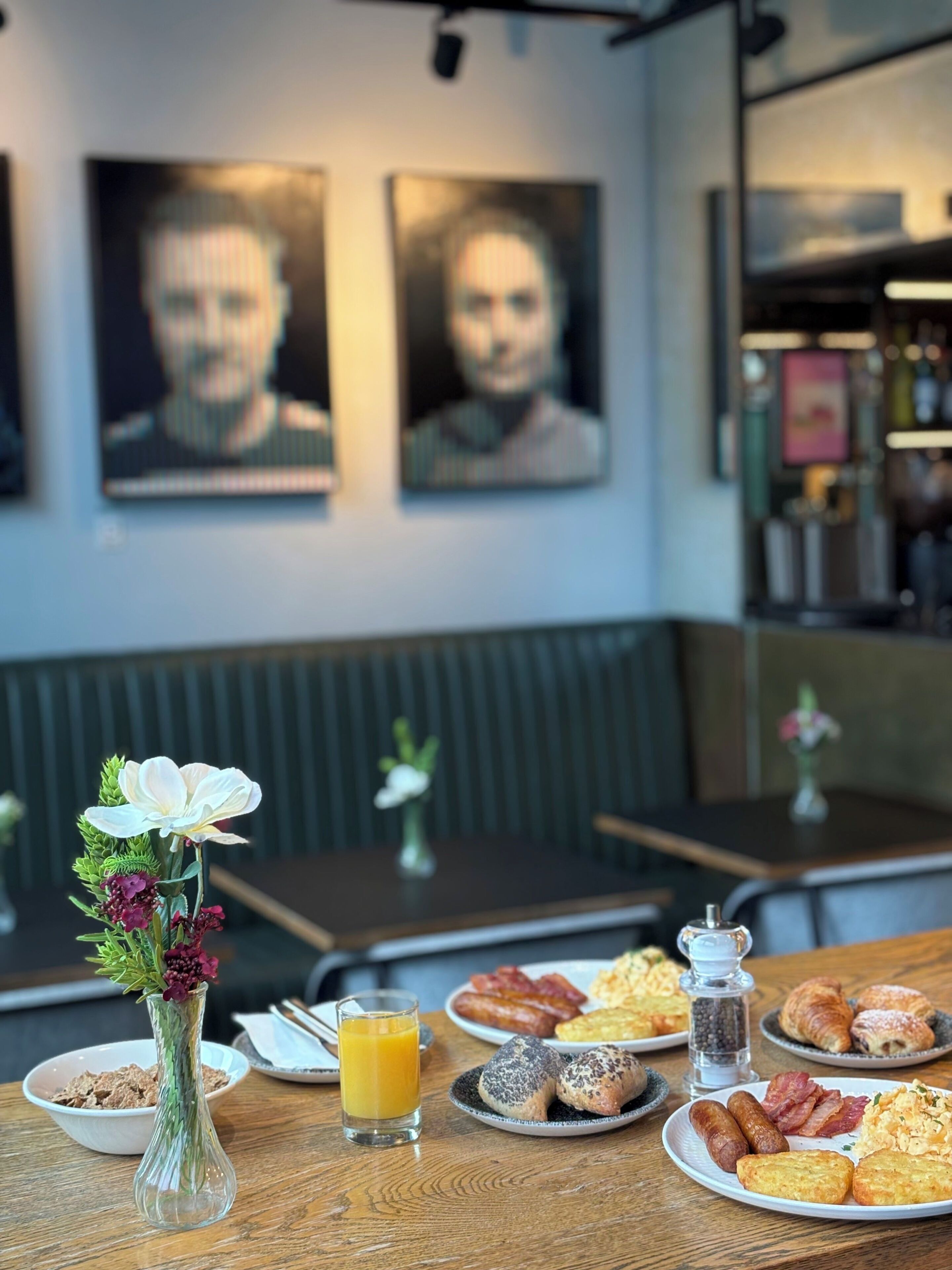 A breakfast setting with a table, a vase with flowers, and a glass of orange juice.