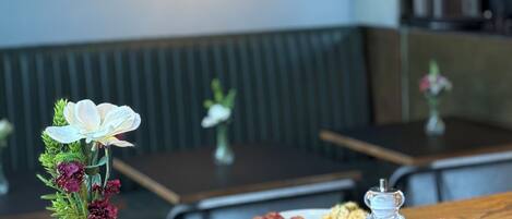 A breakfast setting with a table, a vase with flowers, and a glass of orange juice.