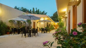 An outdoor patio area with tables and chairs, umbrellas, and potted plants. - Paguro Villa (Ukulhas)