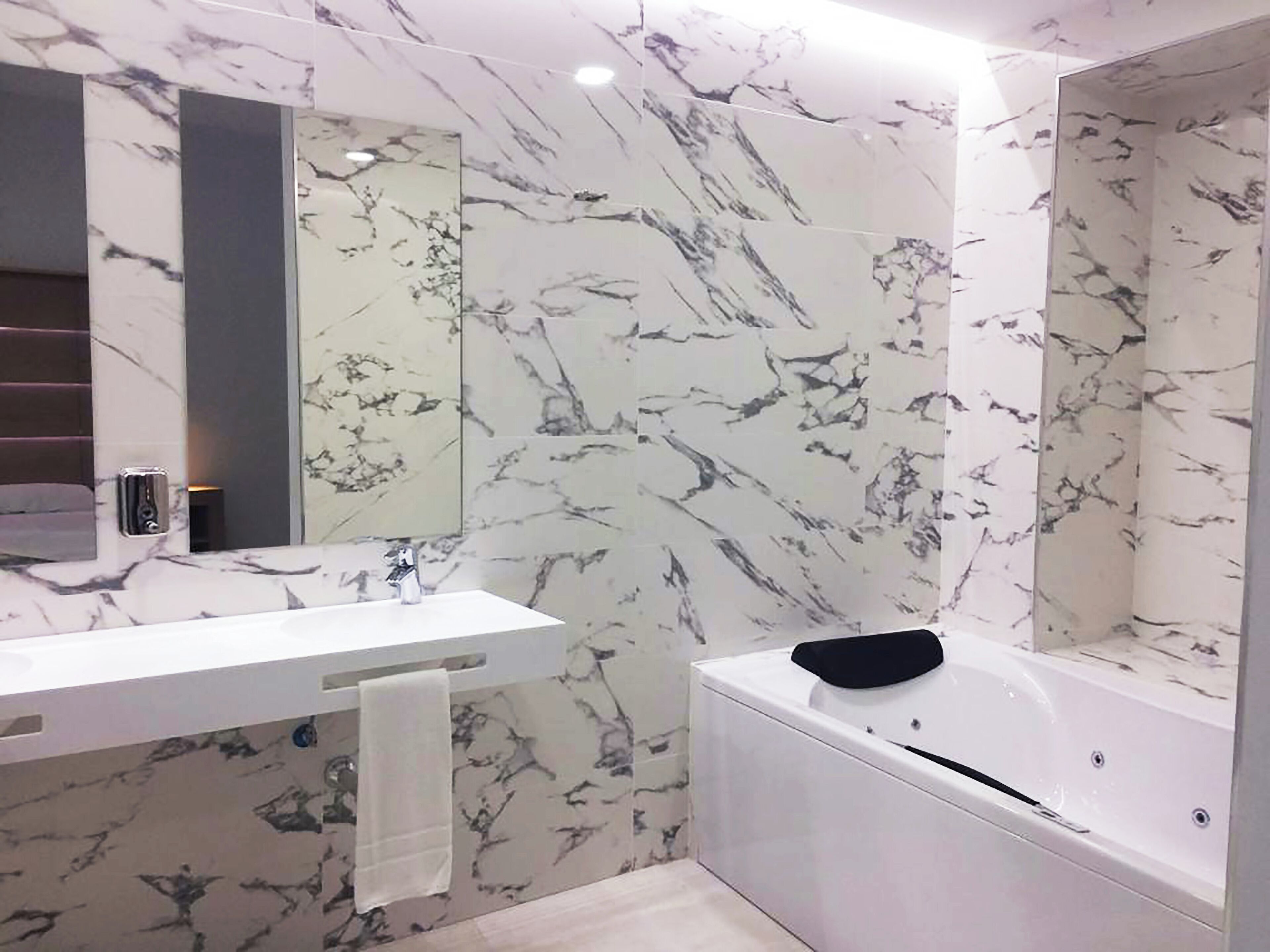 A modern bathroom with a marble backsplash, a white sink, a mirror, and a bathtub.