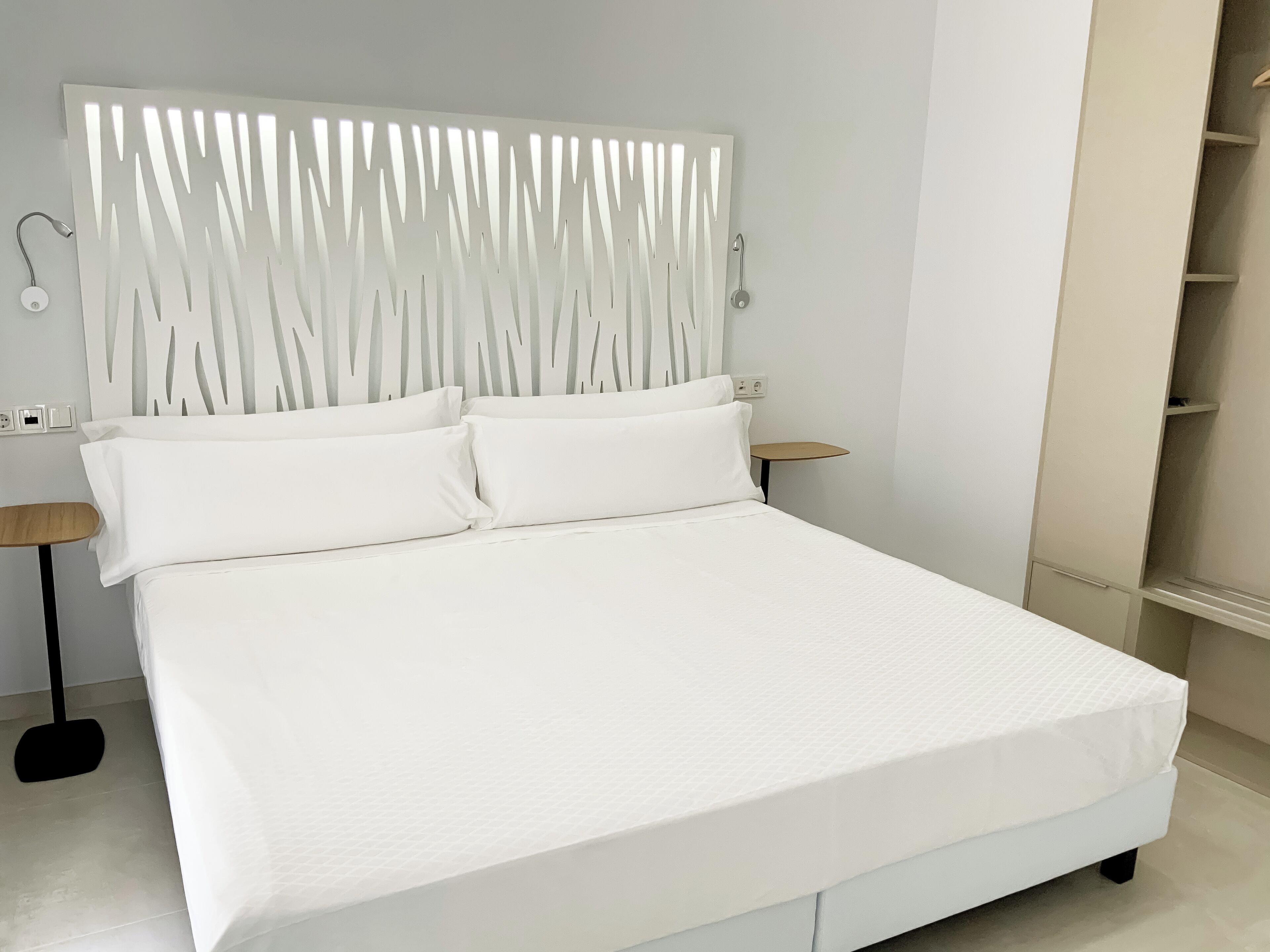 Ein modernes Schlafzimmer mit einem großen Bett, weißer Bettwäsche, einem einzigartigen Kopfteil, Nachttischen und einem eingebauten Kleiderschrank.