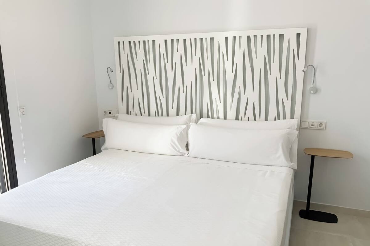 A modern bedroom with a large bed, white bedding, a unique wall panel, and two bedside tables.