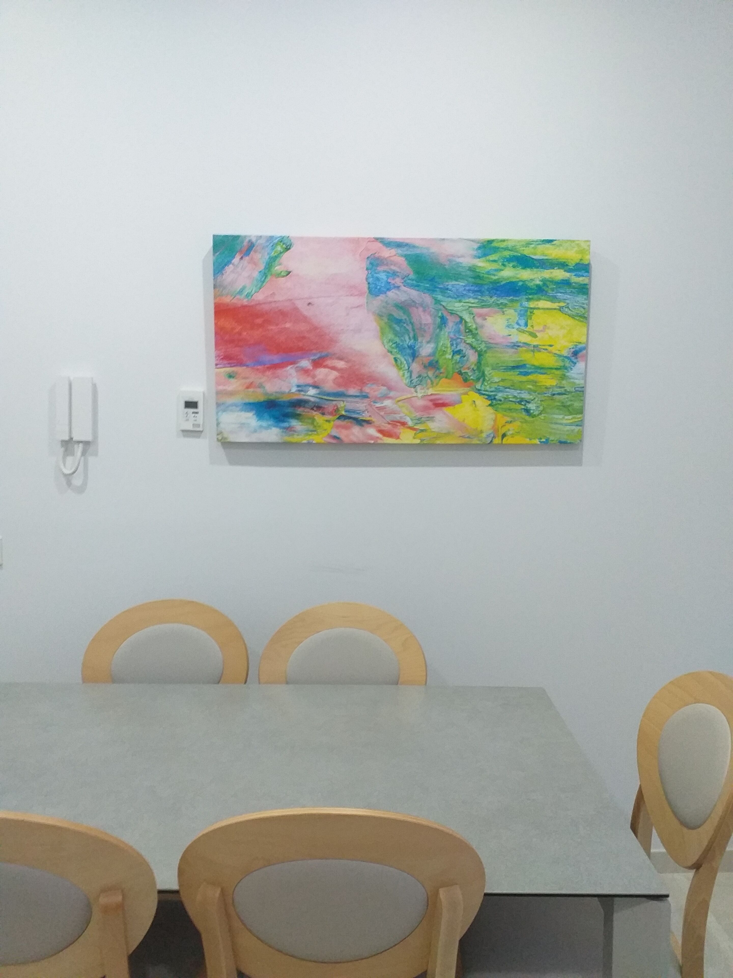 Un salón de conferencias con una mesa gris y sillas de madera. Un cuadro abstracto y colorido está en la pared.