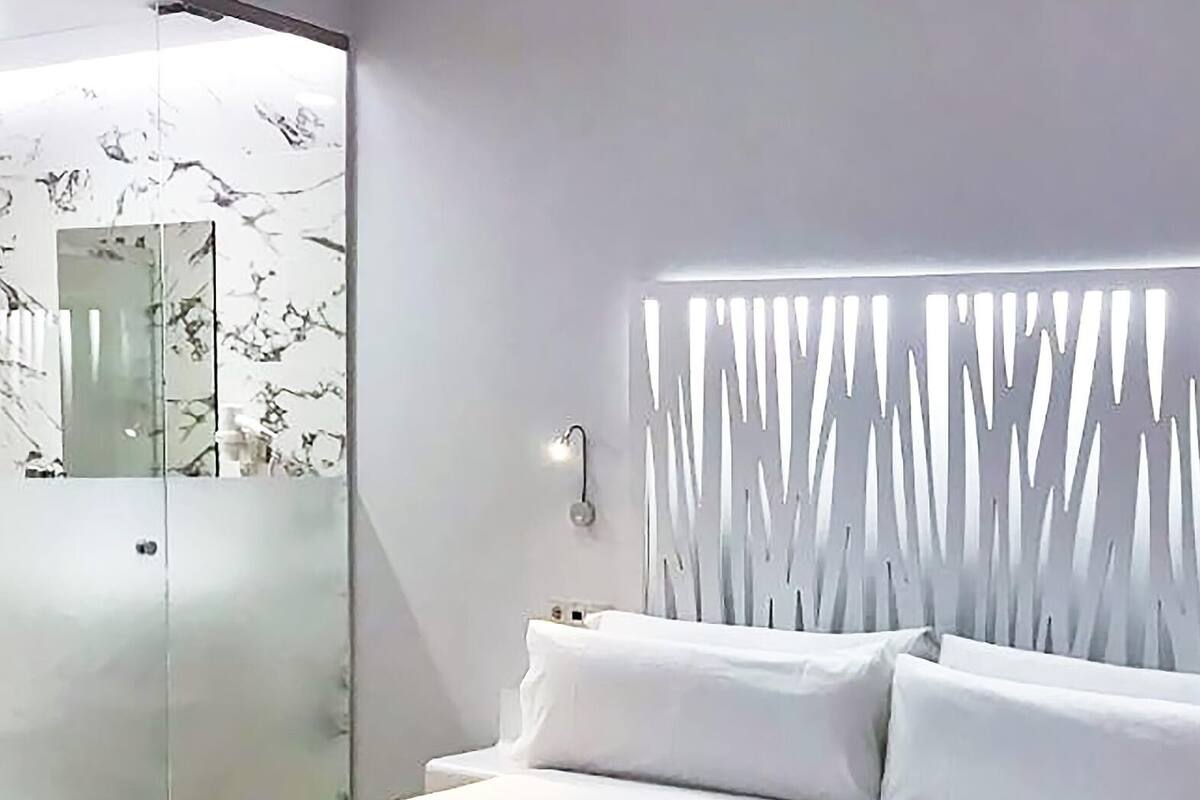 A modern bedroom with a large bed, a glass shower enclosure, and a unique wall panel design.