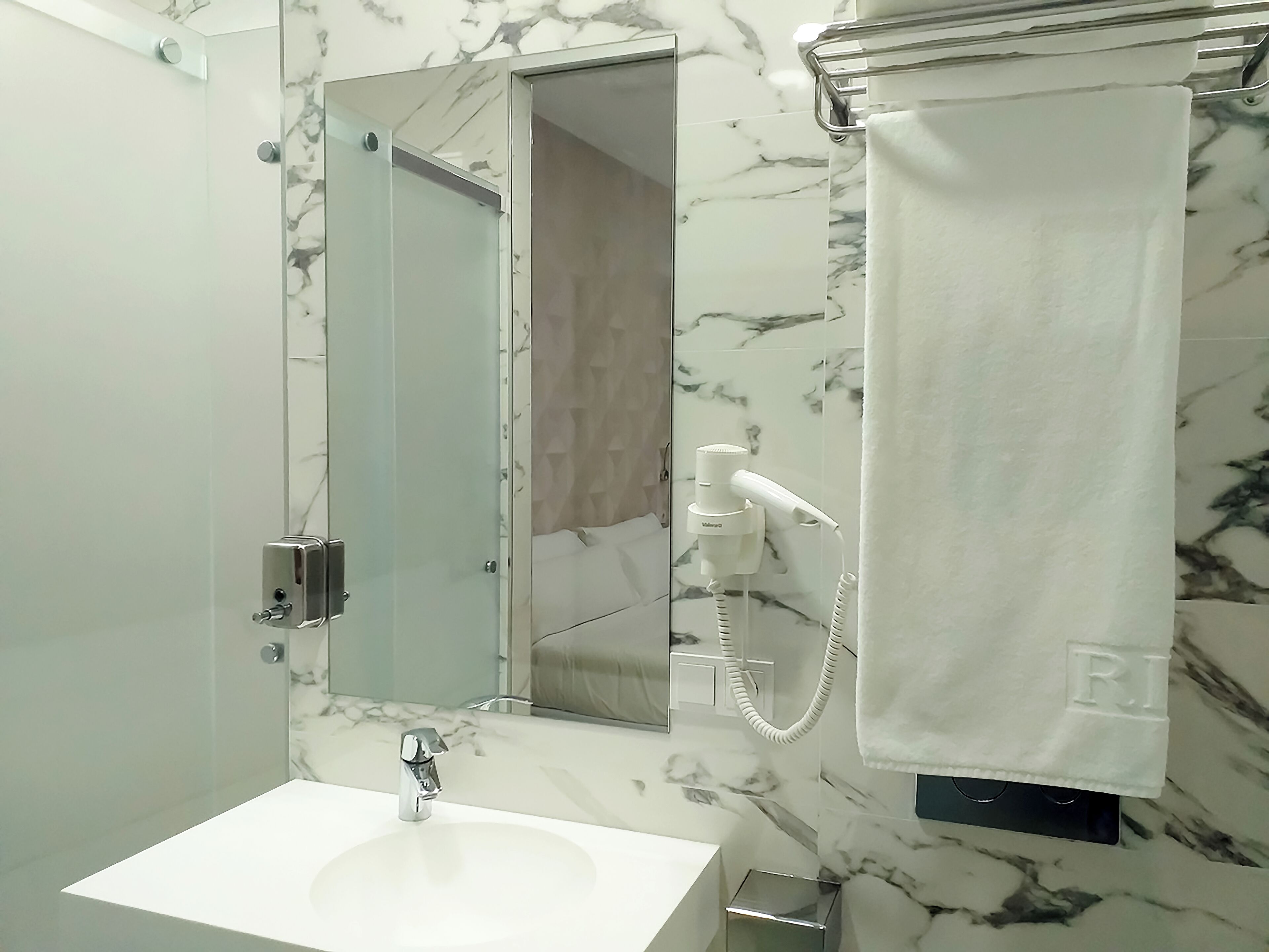 Un baño con un lavamanos blanco, un cabezal de ducha de mano y una toalla colgada en un perchero.