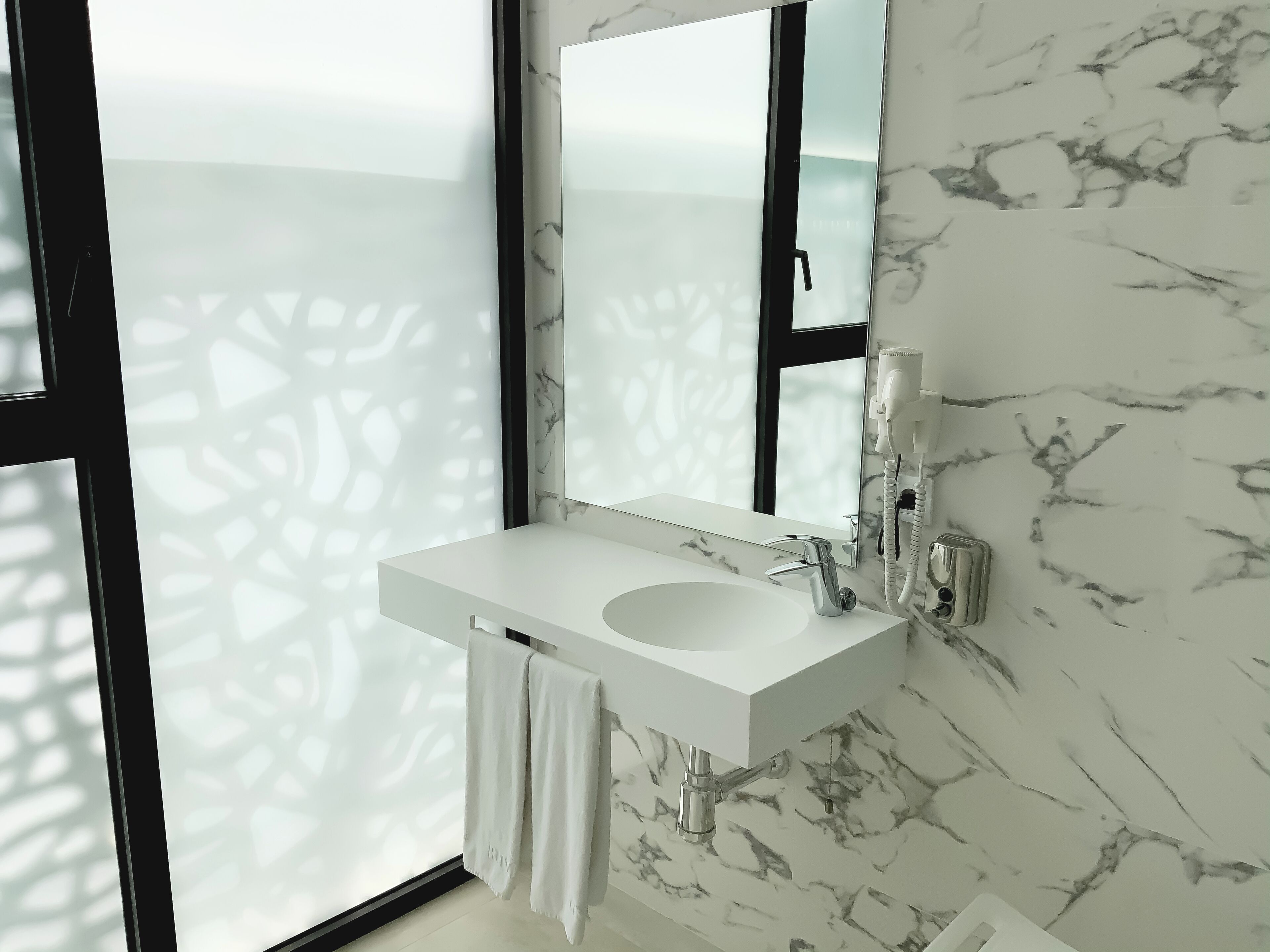 Une salle de bain avec un lavabo en marbre blanc, un grand miroir et une serviette suspendue à un porte-serviettes.