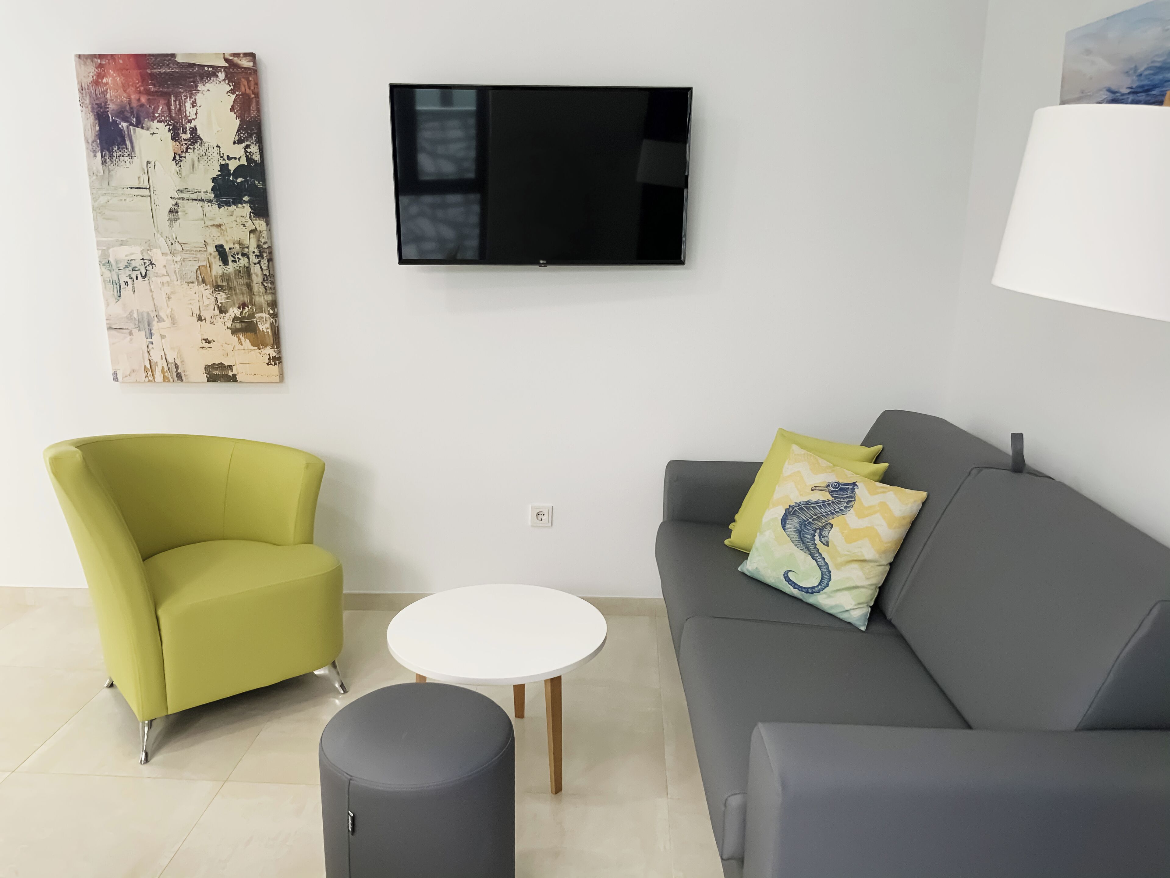 En moderne stue med en grøn lænestol, en grå sofa med pyldepuder, et lille hvidt bord og en grå skammel.