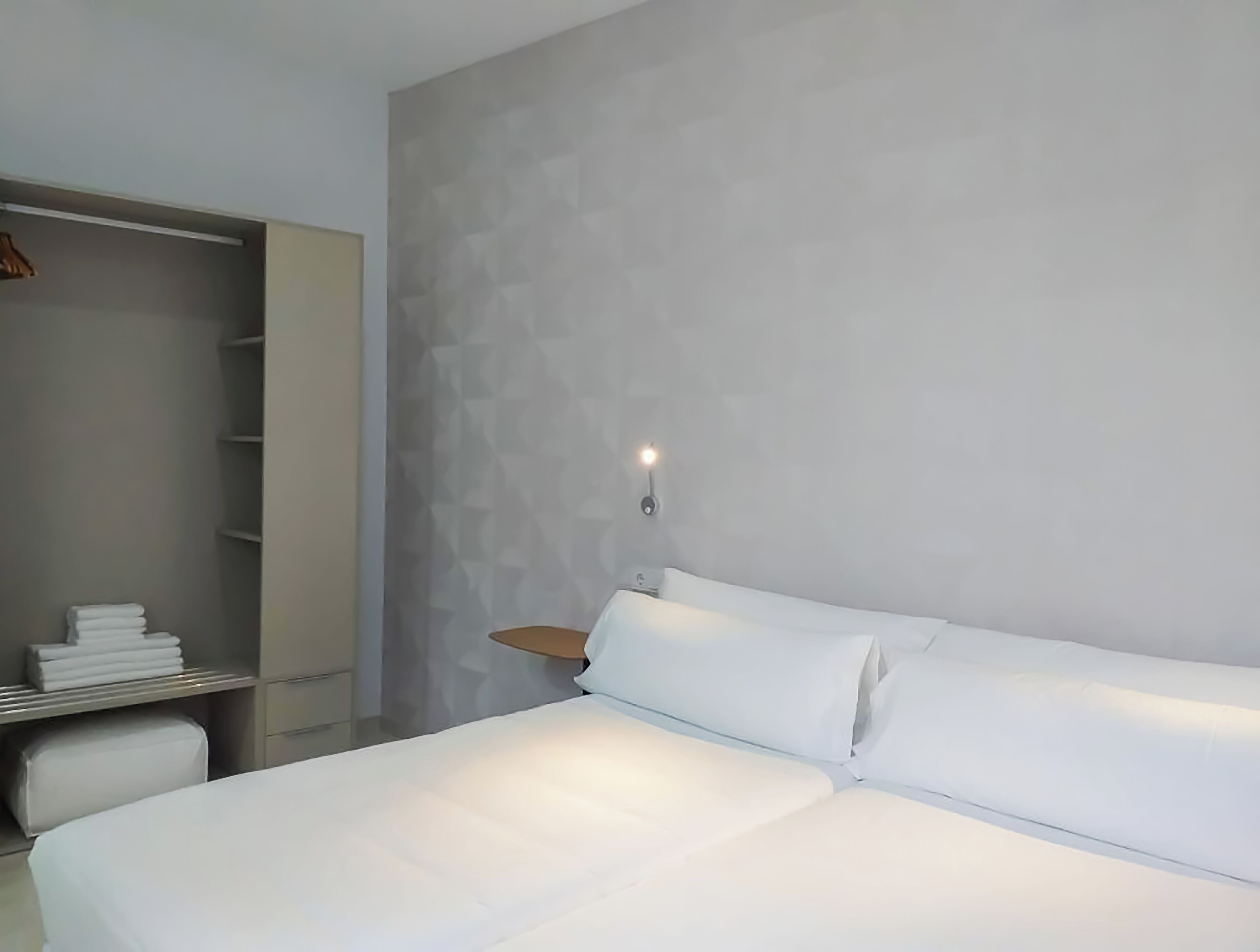 A modern bedroom with a large bed, a built-in wardrobe, and a wall-mounted light fixture.