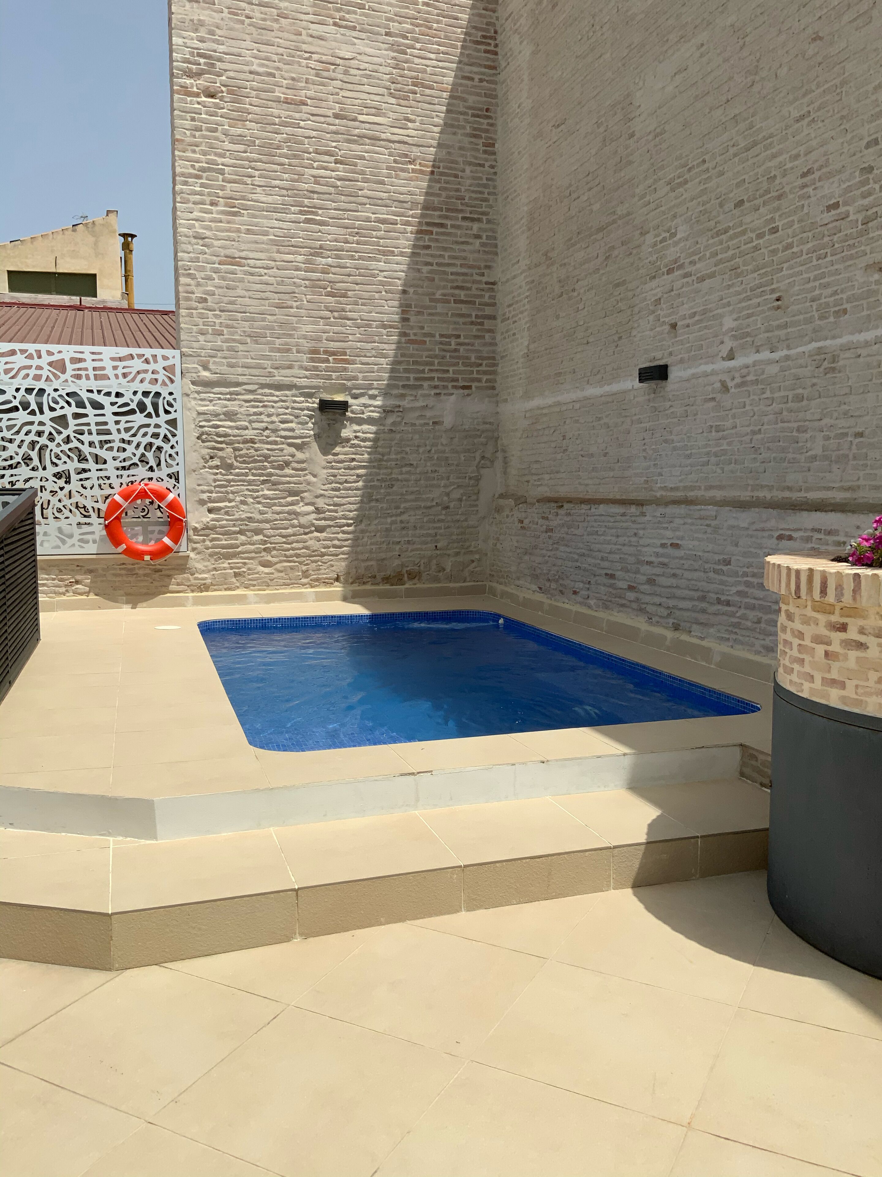 A swimming pool with a tiled deck, a brick wall, and a decorative white panel with a lifebuoy.