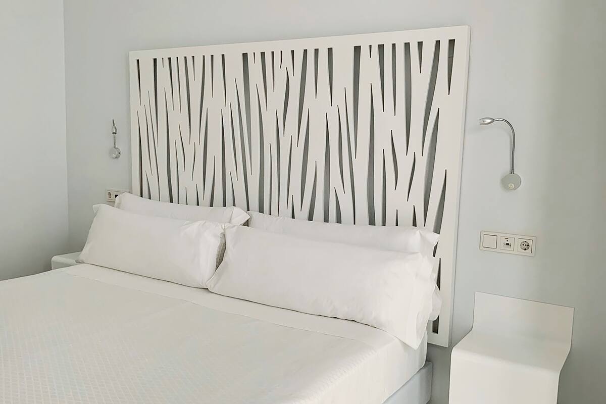 A modern bedroom with a white bed, a unique headboard design, a bedside table, and a wall-mounted light fixture.