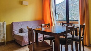 A dining area with a wooden table and chairs, a sofa, and a view of a mountainous landscape through a large window. - Apartamentos Canillo Ribagrossa 3000 (Canillo)