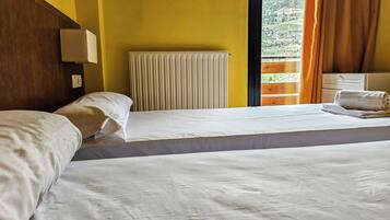 A hotel room with two beds, a radiator, a window with curtains, and a view of a mountainous landscape.