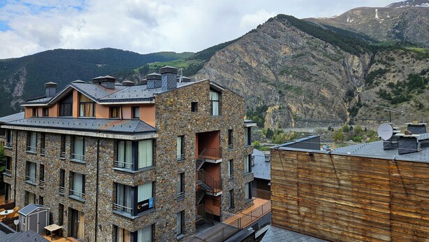 A multi-story building with stone and wood exteriors, balconies, and a view of mountains. - Apartamentos Canillo Ribagrossa 3000 (Canillo)