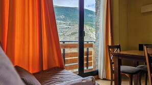 A room with a bed, a wooden table, and a view of a mountainous landscape through an open door. - Apartamentos Canillo Ribagrossa 3000 (Canillo)