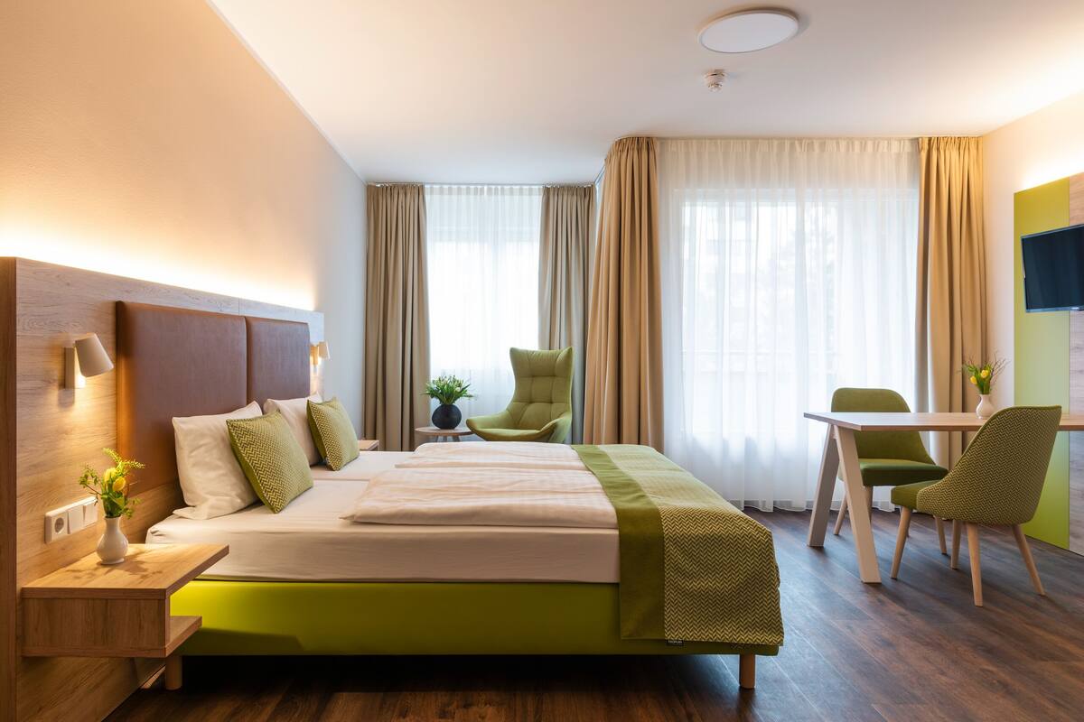 A hotel room with a bed, bedside tables, a desk, chairs, and a television.