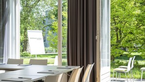 A conference room with a table, chairs, and a view of greenery outside. - Gästehaus Lazarus (Berlin)