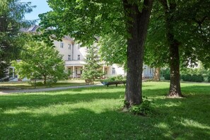 A park with a large tree, a bench, and a building with a balcony in the background. - Gästehaus Lazarus (Berlin)